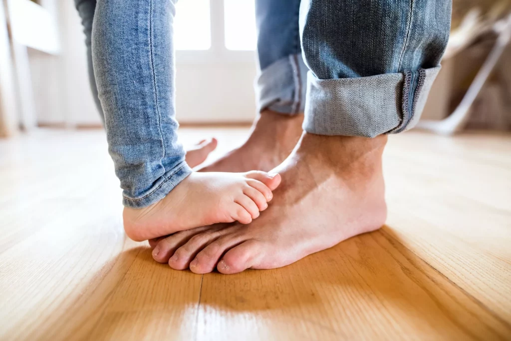 Kinderfüße stehen auf Vaters Füßen auf einem warmen Holzboden